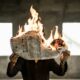 Mann hält brennende Zeitung im Querformat vor das Gesicht.