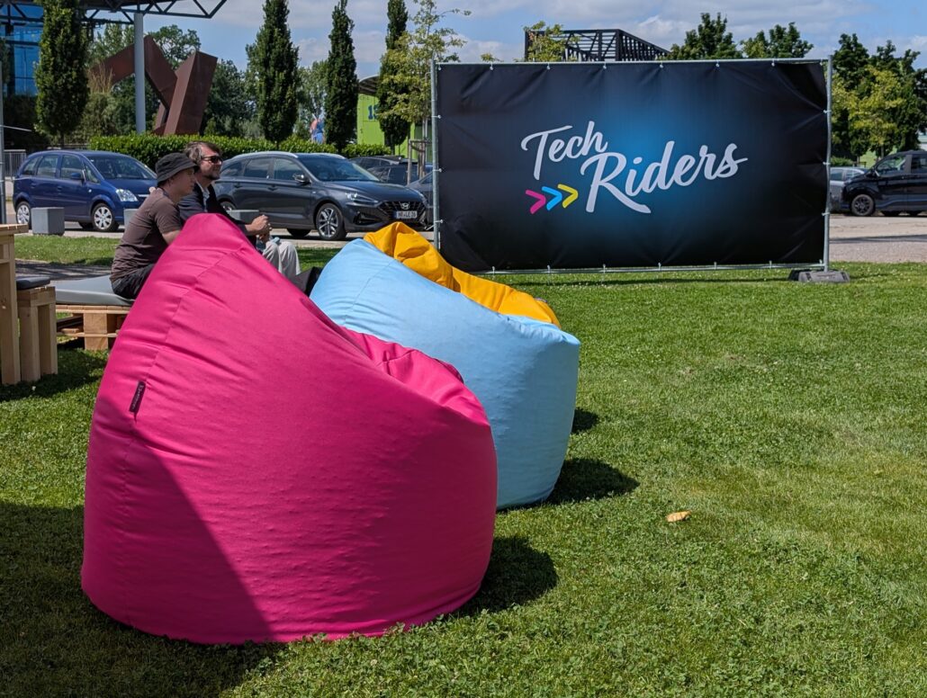 Bunte Sitzsäcke vor einem Sichtschutz mit TechrRiders Logo