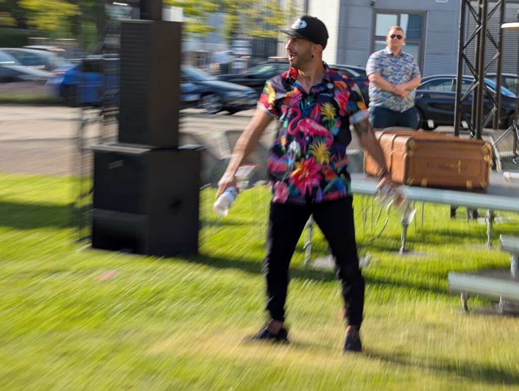 Barkeeper im geblümten Hemd auf der Wiese vor der Bühne jongliert mit Flaschen und Mixer.