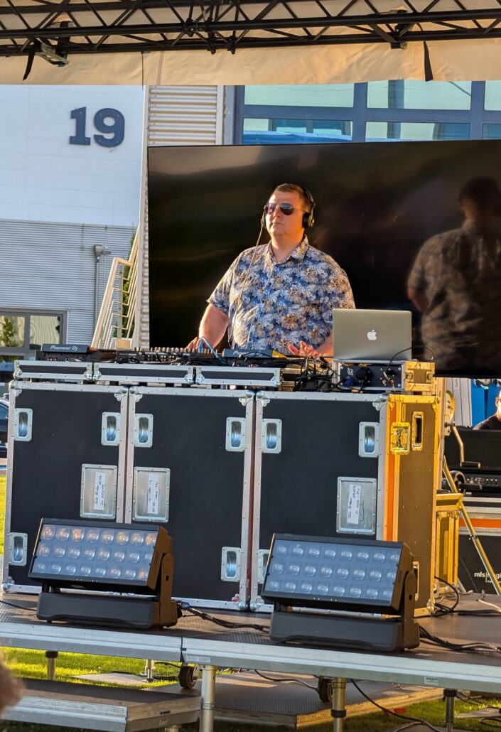 DJ im Hawaihemd mit Sonnenbrille hinter Mischpult.